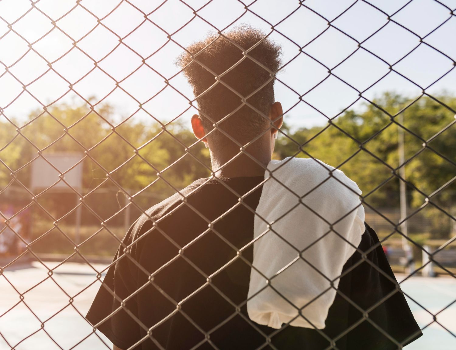 Person standing behind chain-link fence, white towel on shoulder, looking away. Juvenile Defense in Nashville, Tennessee