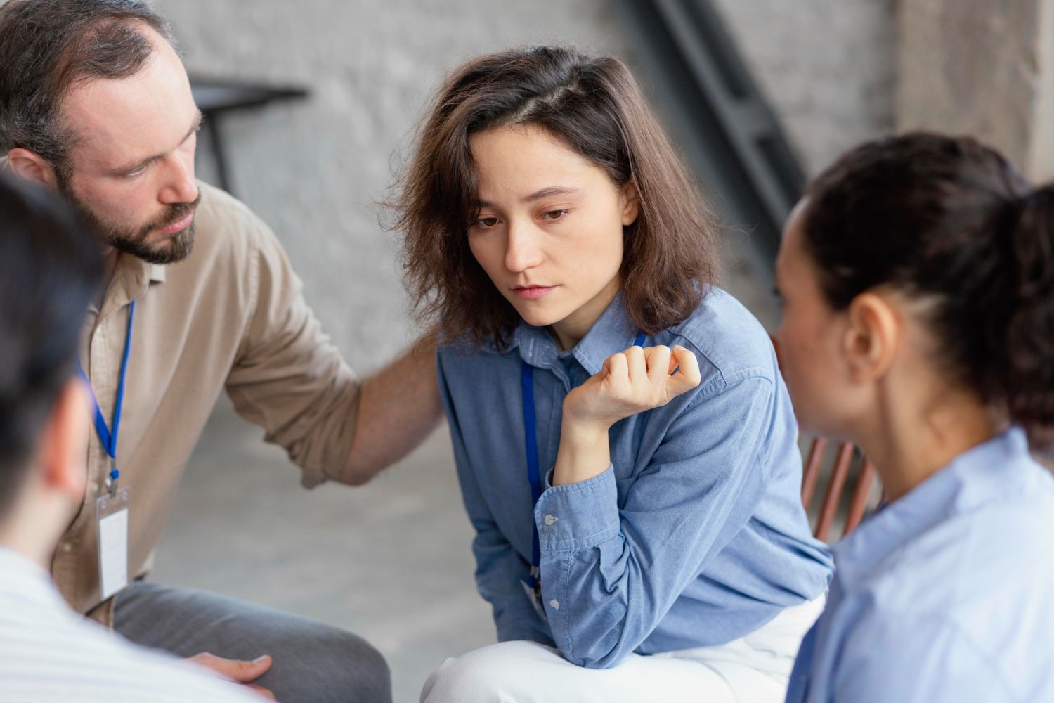A woman in a blue shirt looks down while in a group, a person comforts her. Tennessee Vulnerable Persons Abuse Registry  in Nashville, Tennessee