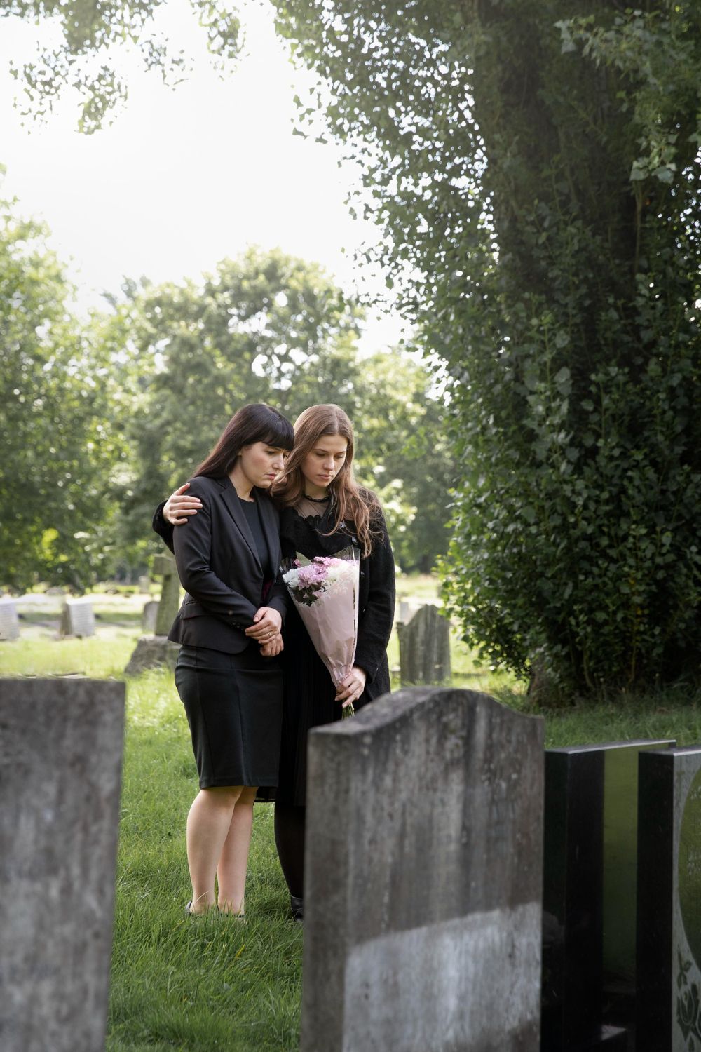 Two women at a gravesite; one with arm around the other, holding flowers, expressing grief. Wrongful Death in Nashville, Tennessee