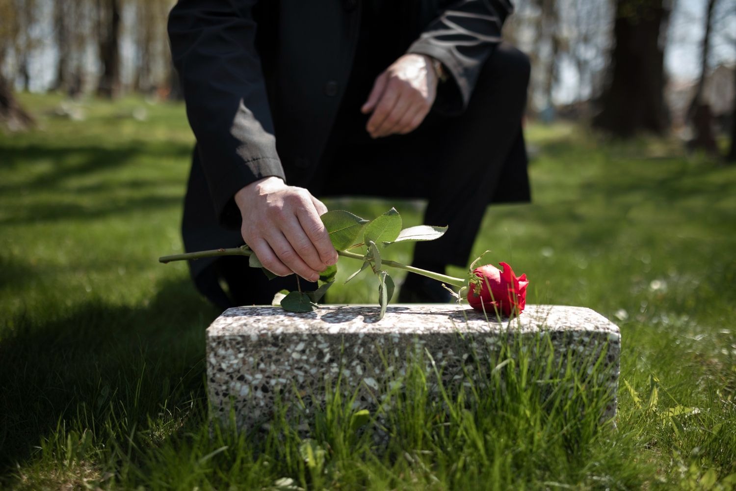 Person placing a red rose on a tombstone in a grassy cemetery. Wrongful Death in Nashville, Tennessee