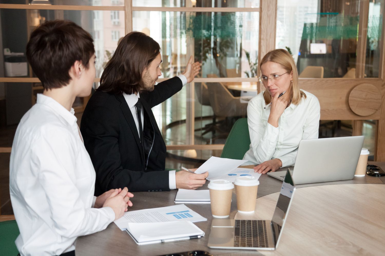 Three people in a business meeting. A man gestures at papers, looking frustrated; two women look on, one thoughtful. Commercial Disputes in Nashville, Tennessee