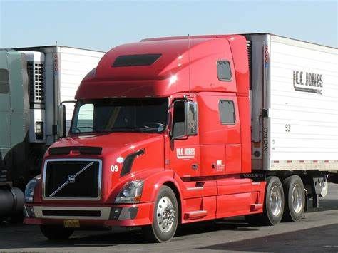 Red semi-truck with white trailer, parked outdoors in daylight. 