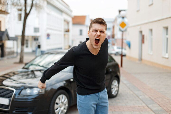 Man yelling next to black car on city street. He wears black top and blue jeans, with angry expression. Reckless Driving in Nashville, Tennessee