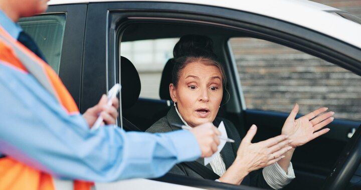 Woman in car looking surprised, gesturing with hands; person in orange vest outside car. Traffic Violations / CDL in Nashville, Tennessee