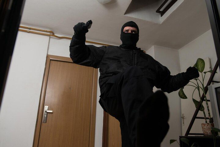 Person in black tactical gear, ski mask, and gloves points a gun indoors. Criminal Trespass in Nashville, Tennessee