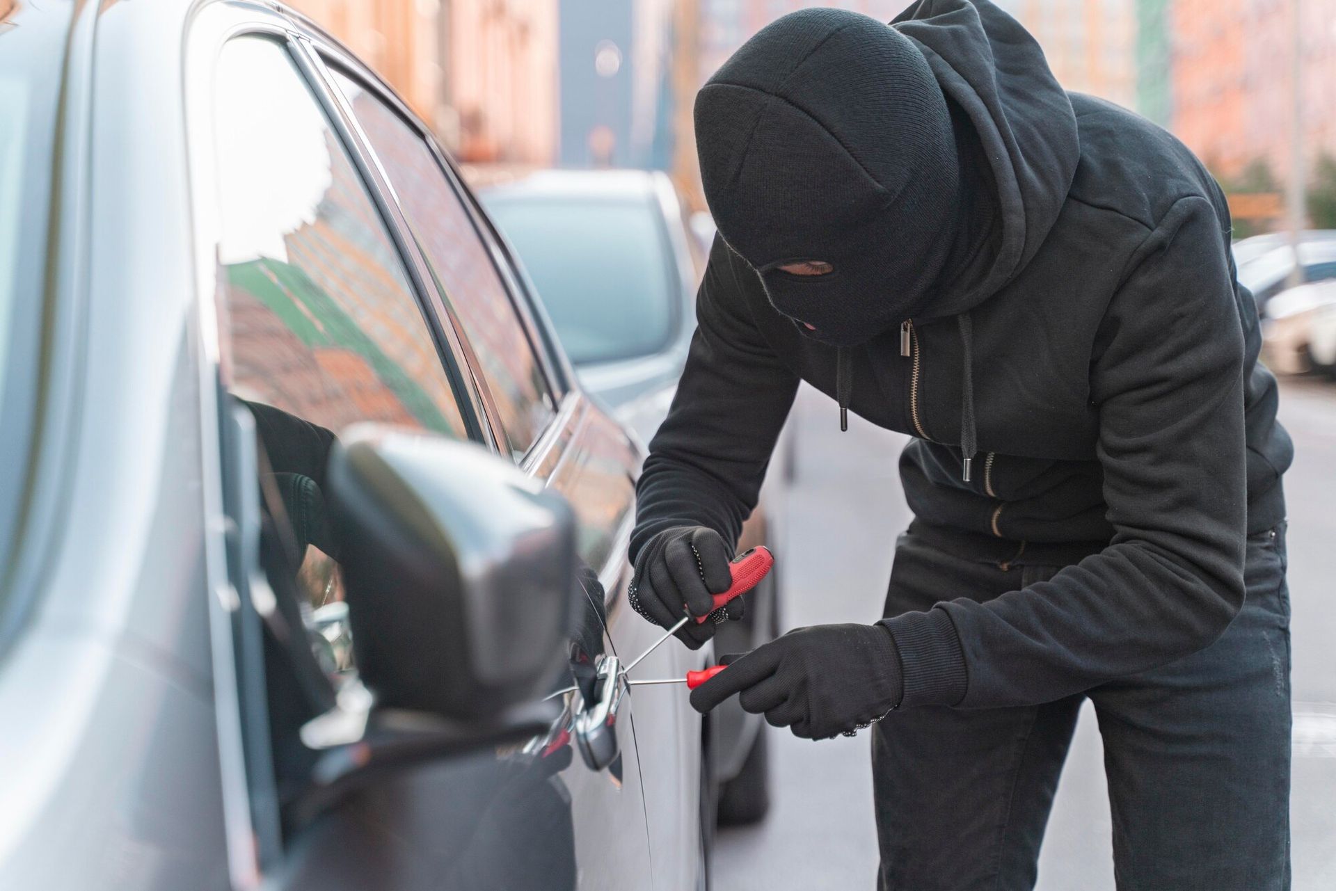 Person in black clothing and balaclava using tools to open a car door. Carjacking in Nashville, Tennessee