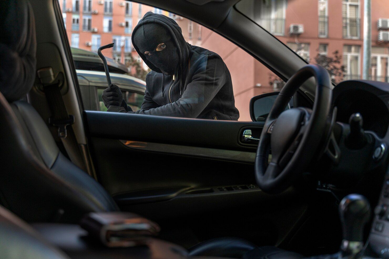 A masked person using a crowbar to break into a car, viewed from inside the vehicle. Robbery in Nashville, Tennessee