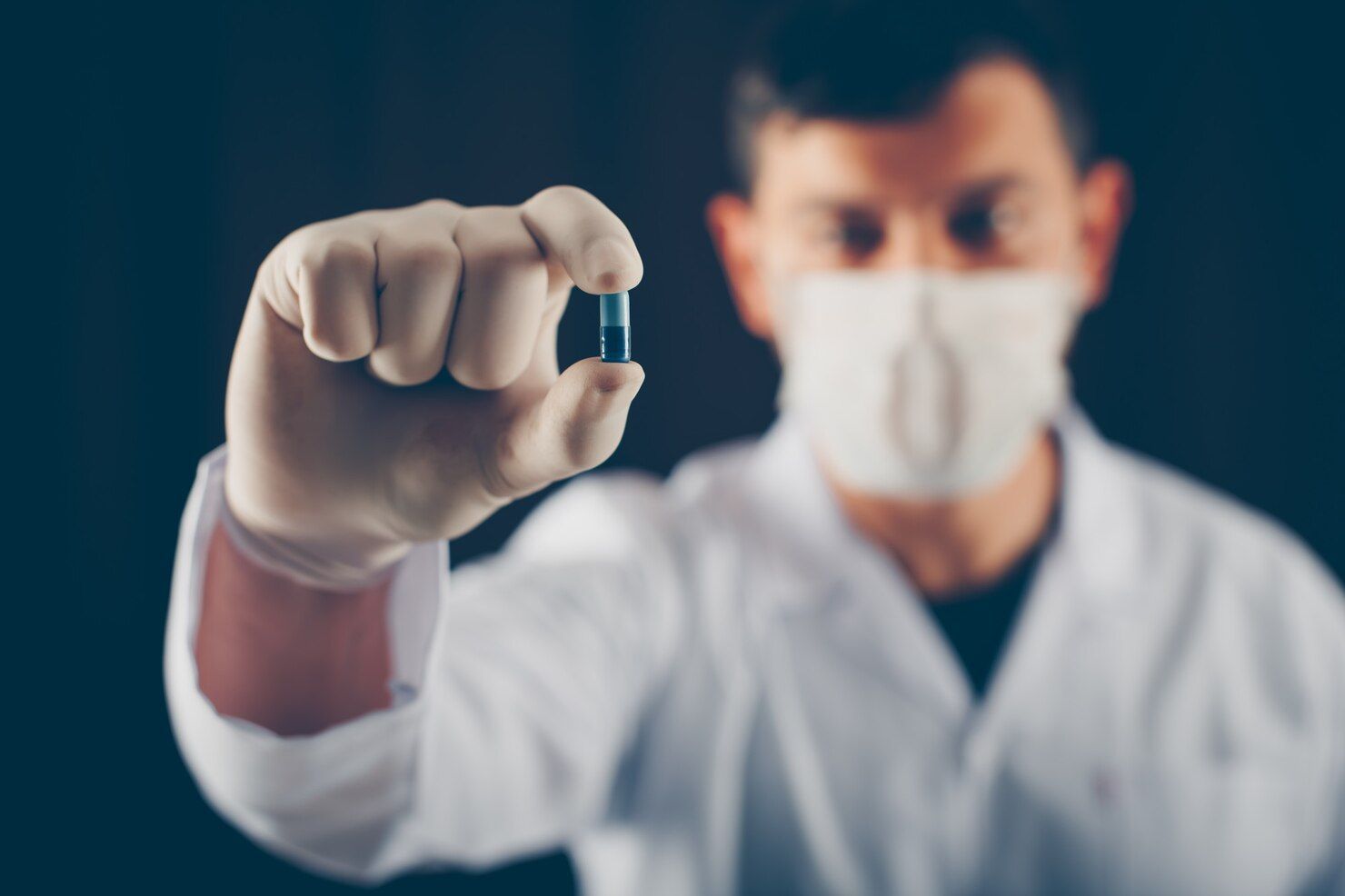 Person in lab coat and mask holding a blue capsule between gloved fingers. Drug Conspiracy in Nashville, Tennessee