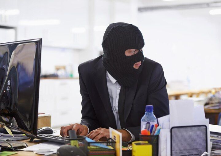 Person in black mask, suit, at a computer, looking to the side. Theft of Services in Nashville, Tennessee