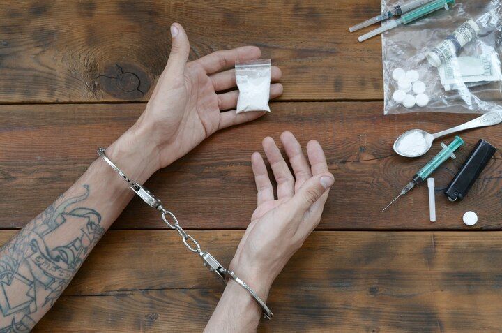 Hands cuffed on a wooden surface, holding a bag of white powder, with drug paraphernalia nearby. Drug Possession in Nashville, Tennessee