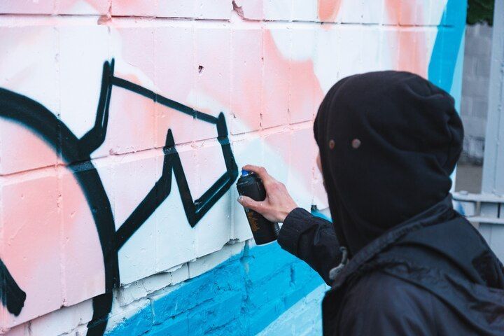 Person in black hoodie spray-painting graffiti on a brick wall, using black paint. Vandalism in Nashville Tennessee