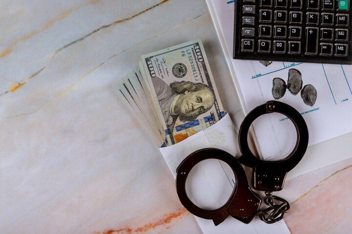 Handcuffs, money, calculator, and papers on a marble surface, suggesting financial crime. Embezzlement Charges in Nashville, Tennessee