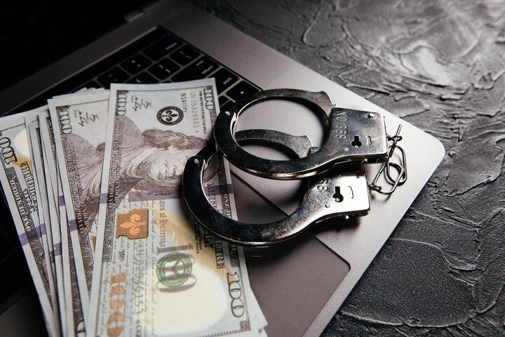 Handcuffs and cash on a laptop, suggesting a crime or financial investigation. Embezzlement Charges in Nashville, Tennessee