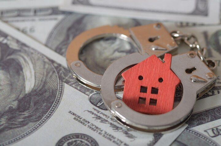 Handcuffs around a red house model on a bed of US dollar bills. Property Crimes in Nashville, Tennessee