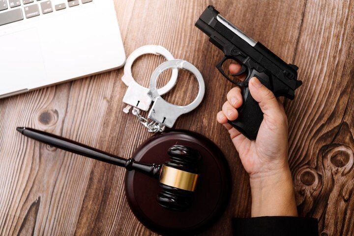 Hand holding a handgun, handcuffs, gavel, and laptop on a wooden surface. Weapons Charges in Nashville, Tennessee