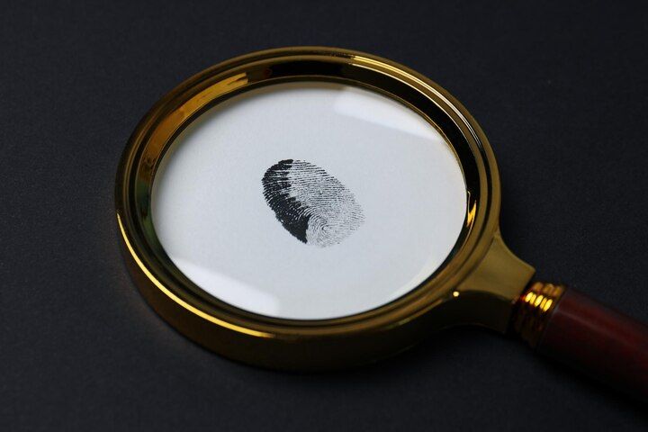 Magnifying glass over a fingerprint on white surface; gold frame, dark background. Identity Theft in Nashville Tennessee