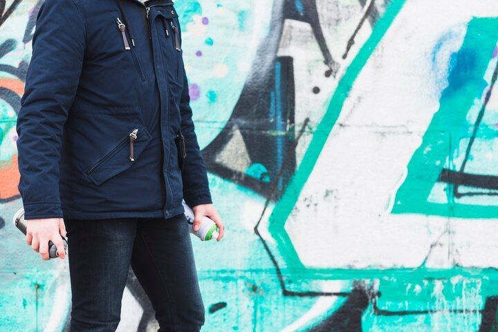 Person with spray paint can stands next to graffiti-covered wall. Vandalism in Nashville, Tennessee