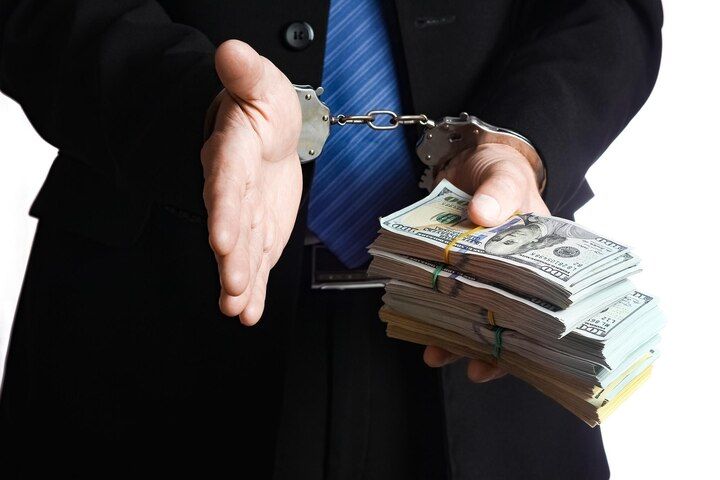 Person in suit handcuffed, offering handshake with one hand and stacks of cash with the other. White Collar & Financial Crimes in Nashville, Tennessee