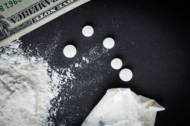 Pills, white powder, and money on a black surface, suggesting illicit drug use and financial transaction. Drug Conspiracy in Nashville, Tennessee