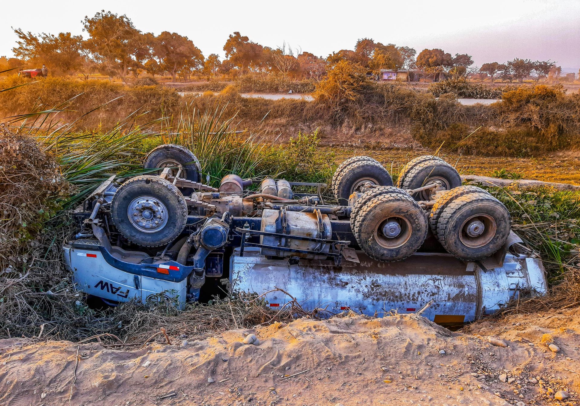 Tanker truck overturned in a ditch, amidst brown vegetation and dirt, with a background of trees. Truck Accidents in Nashville Tennessee