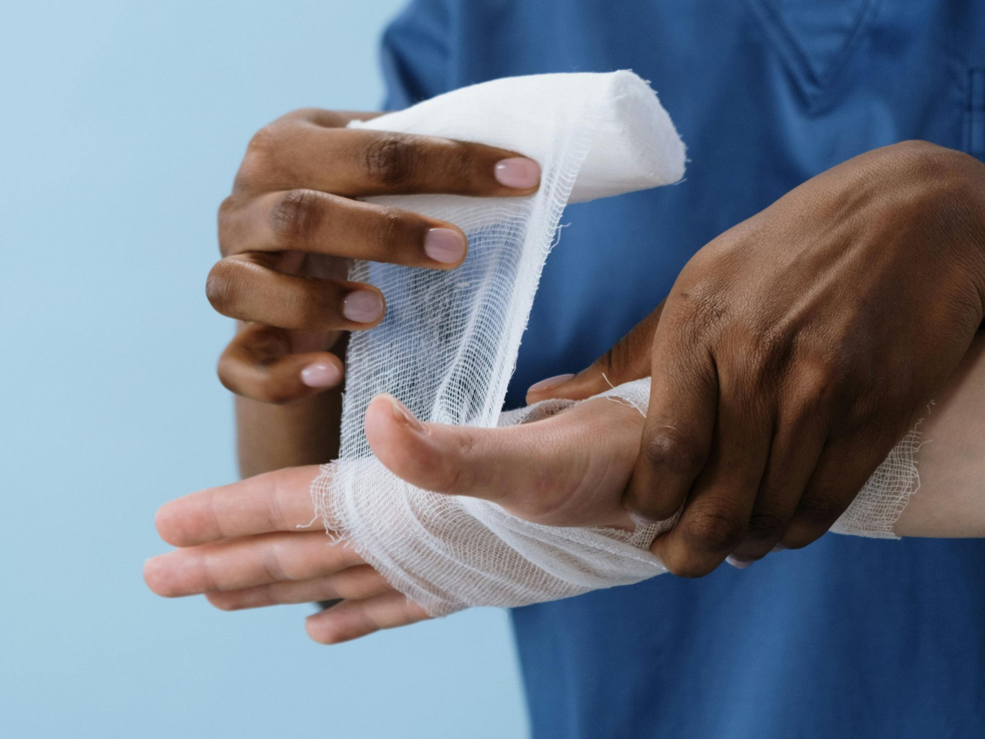 Dark-skinned person bandaging a light-skinned hand with white gauze bandage against a blue background. Personal Injury in Nashville, Tennessee