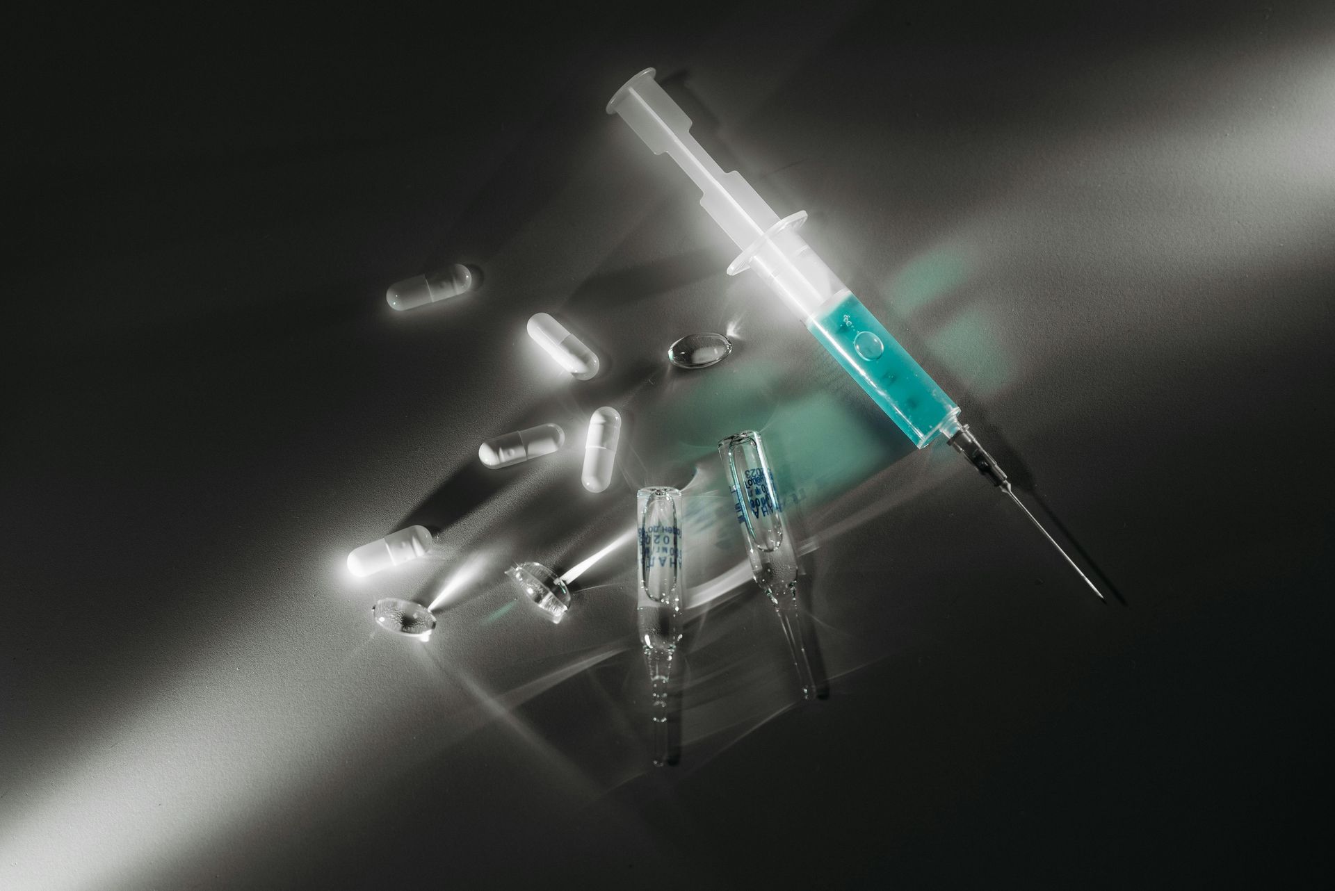 Syringe with blue liquid, pills, and vials on a dark surface, lit from above. Drug Paraphernalia in Nashville, Tennessee
