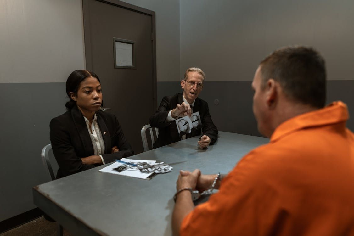 In a jail interrogation room, two people question a handcuffed man in an orange jumpsuit. Freeman & Fuson Trial Lawyers in Nashville, Tennessee