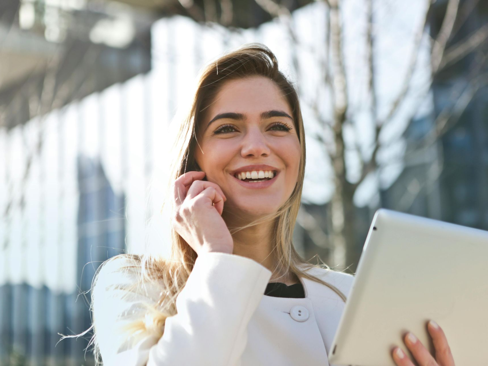Woman smiles while talking on phone and holding a tablet outside a building. Contact Us in Nashville, Tennessee
