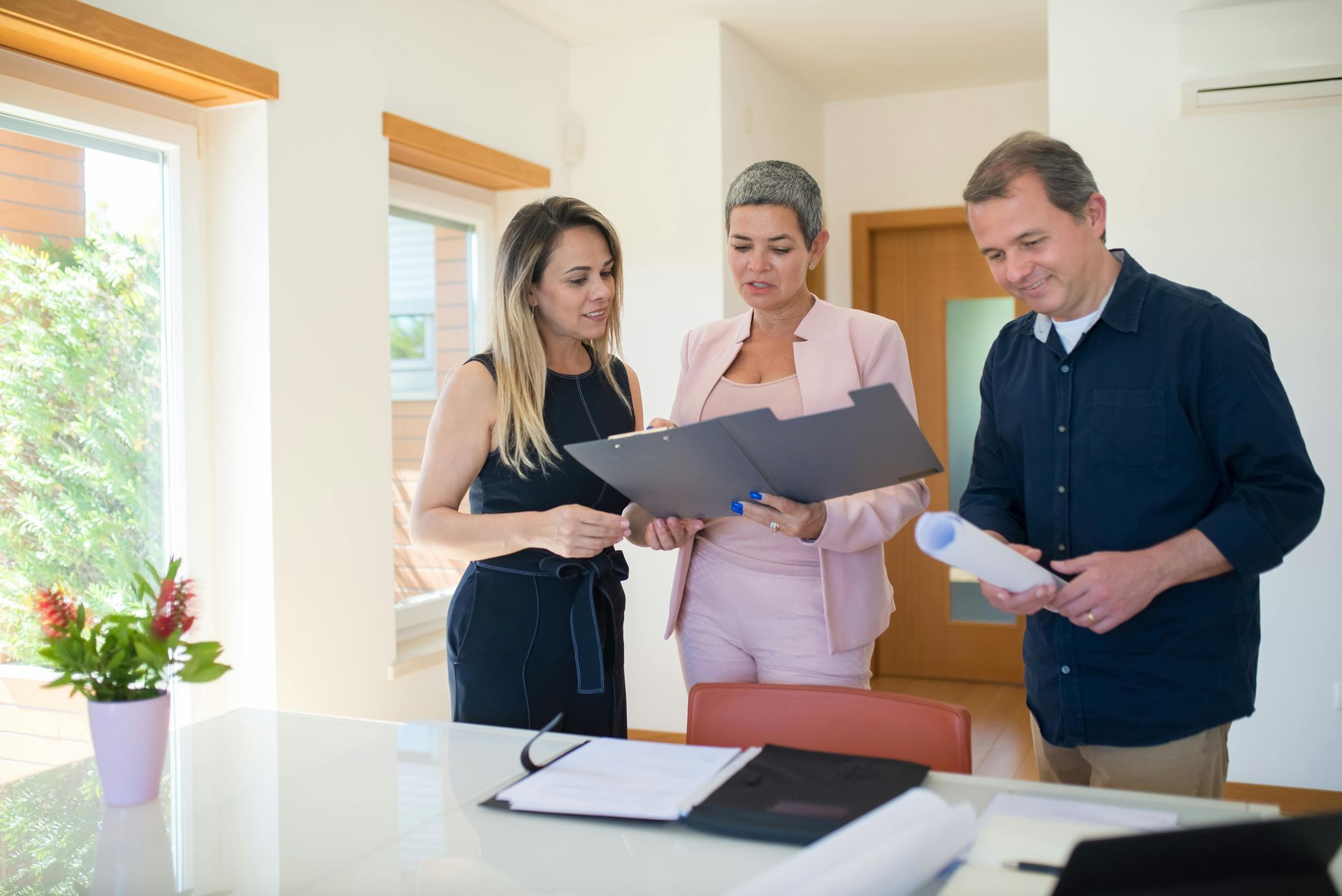 Three people reviewing documents in a light-filled room; a woman in pink holds a folder, others look at plans. Real Estate Disputes in Nashville, Tennessee