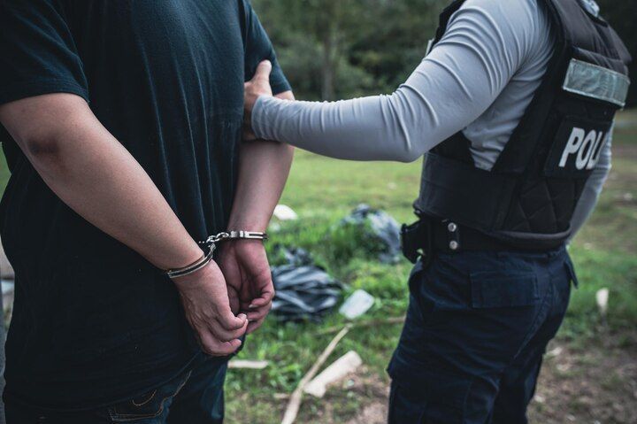 A person in handcuffs is held by a police officer. Outdoors. Voluntary Manslaughter
 in Nashville, Tennessee