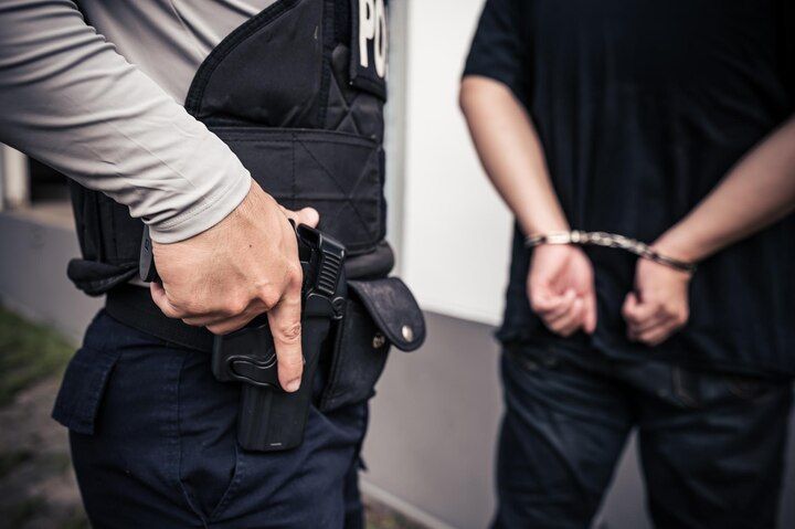 Police officer with a hand on a holstered handgun; person in handcuffs faces away. Voluntary Manslaughter in Nashville, Tennessee