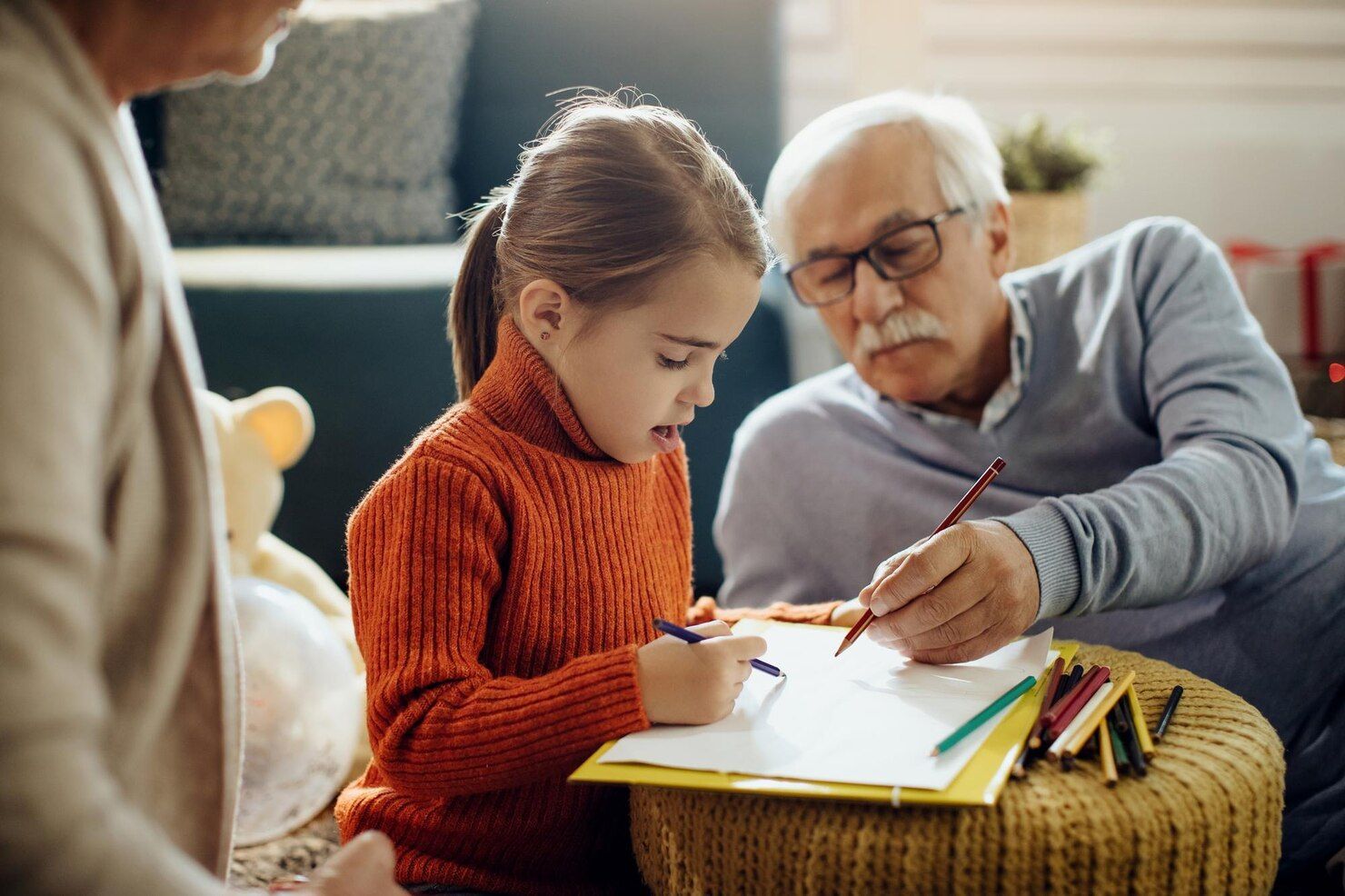 Girl and grandfather draw together, orange sweater, sitting on floor, colored pencils. Grandparent’s Rights in Nashville, Tennessee