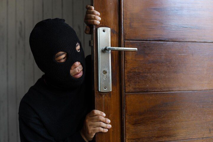 Person in black mask peeking around a wooden door. Burglary in Nashville, Tennessee