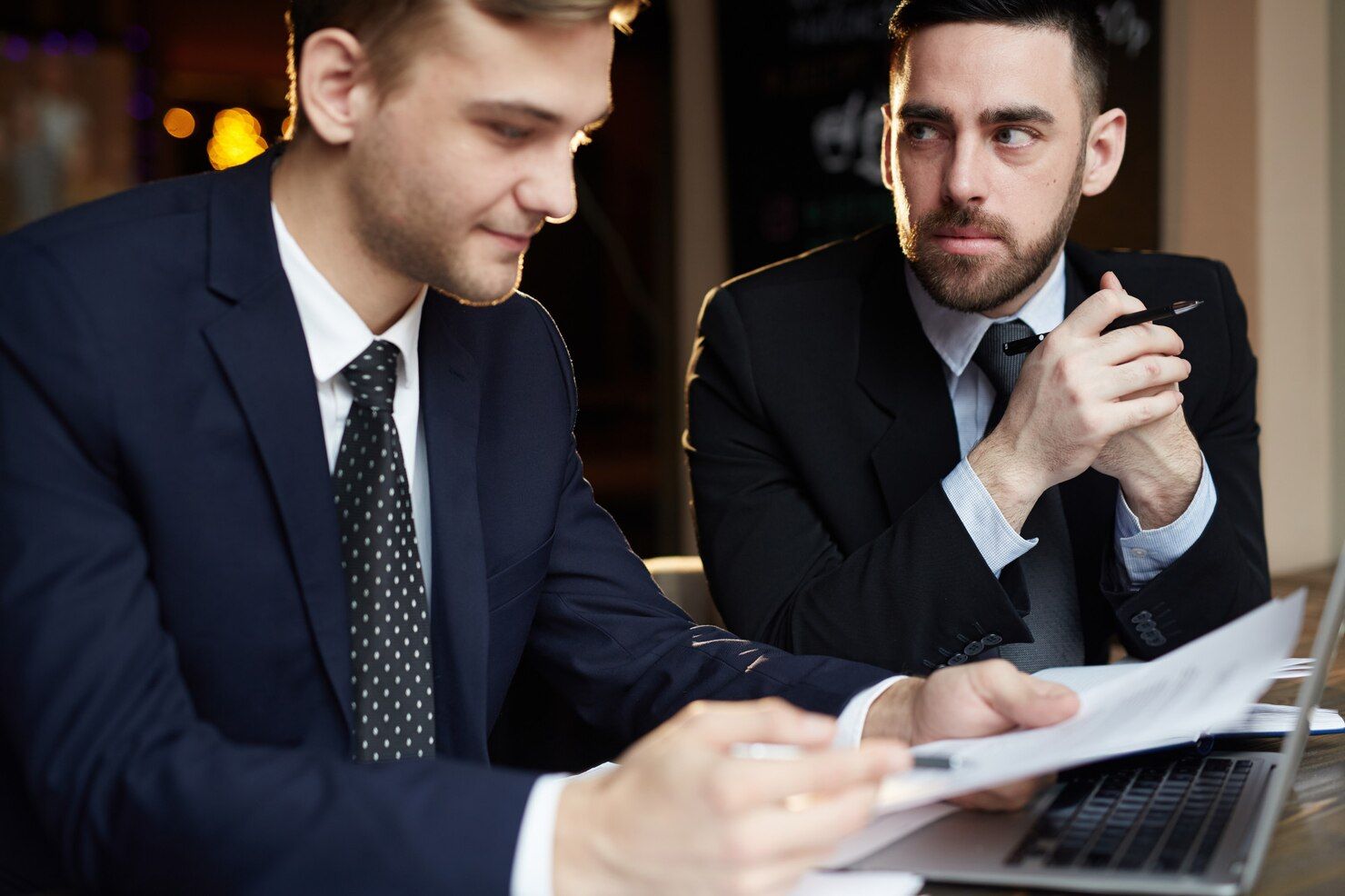 Two men in suits reviewing documents near a laptop; one points while the other looks on thoughtfully. Forgery in Nashville, Tennessee