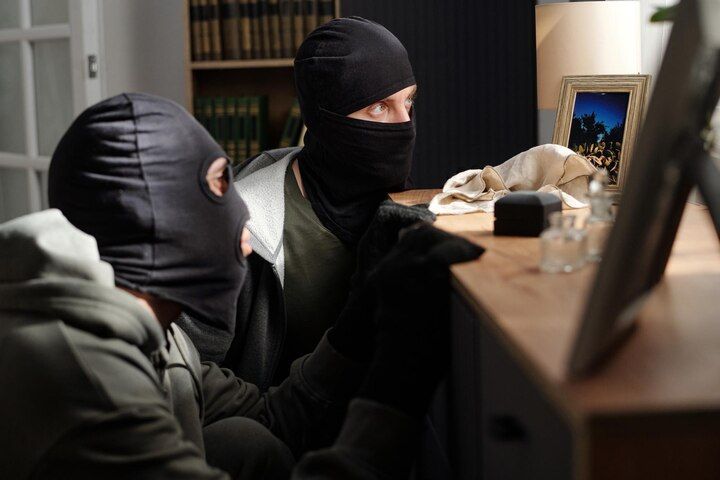 Two people wearing black ski masks examining an object on a table in a dimly lit room. Aggravated Criminal Trespass in Nashville, Tennessee