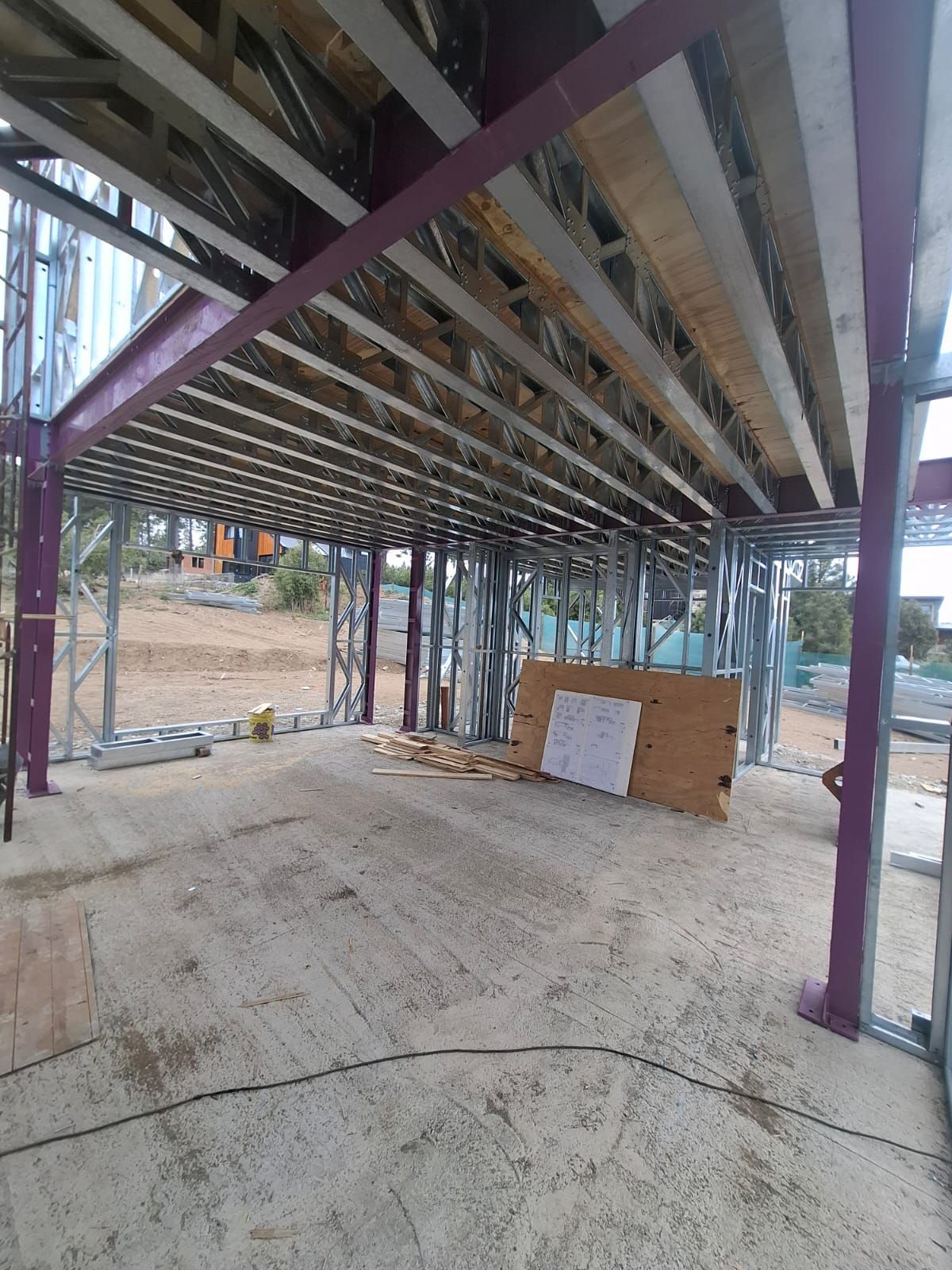 Tres obreros de la construcción, con cascos y chalecos de seguridad, están de pie en una obra, revisando juntos los planos.