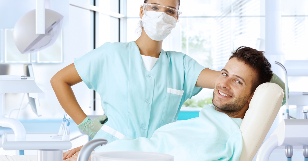 Um homem está sentado em uma cadeira odontológica com uma enfermeira ao lado dele.