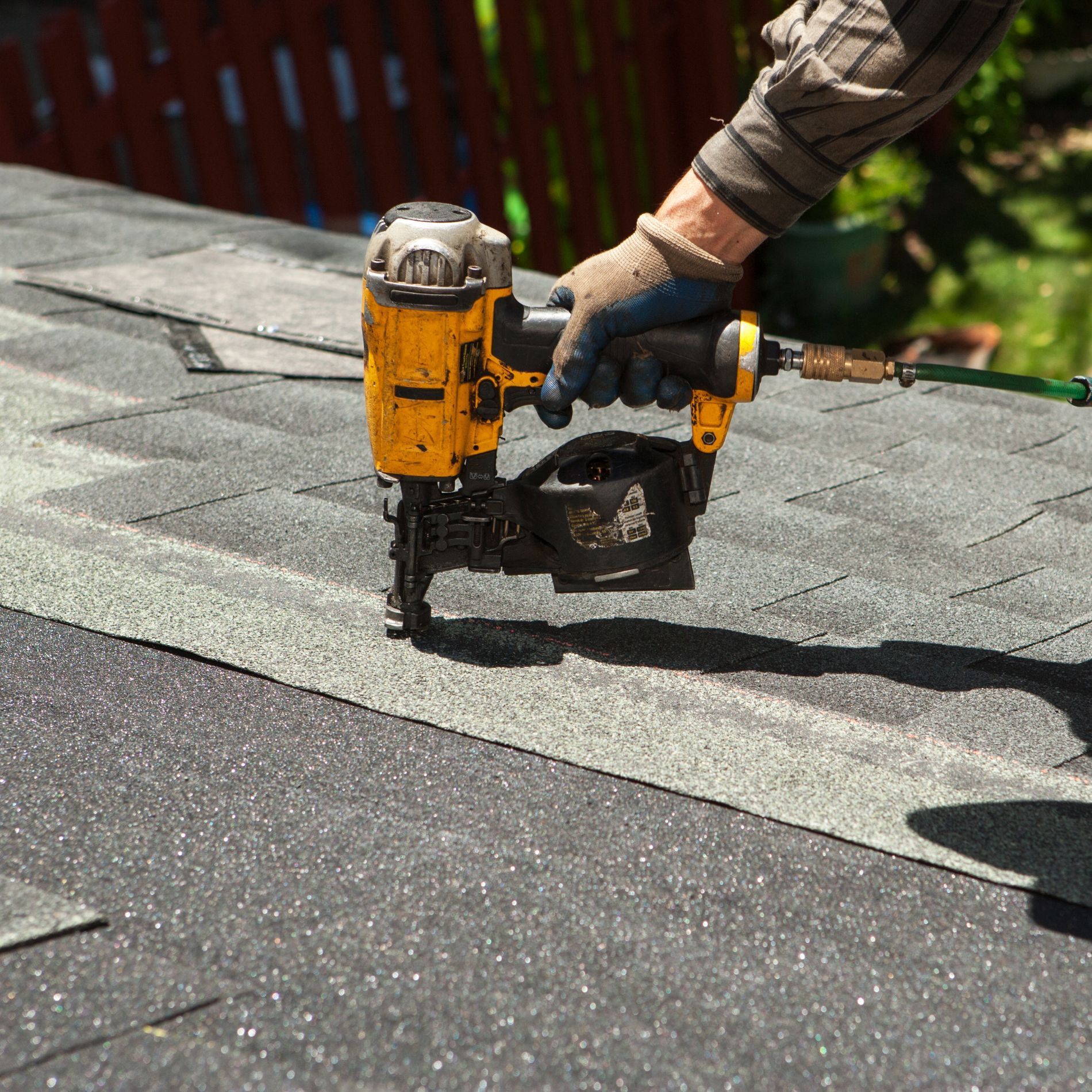 Person using a yellow nail gun to install shingles on a roof.