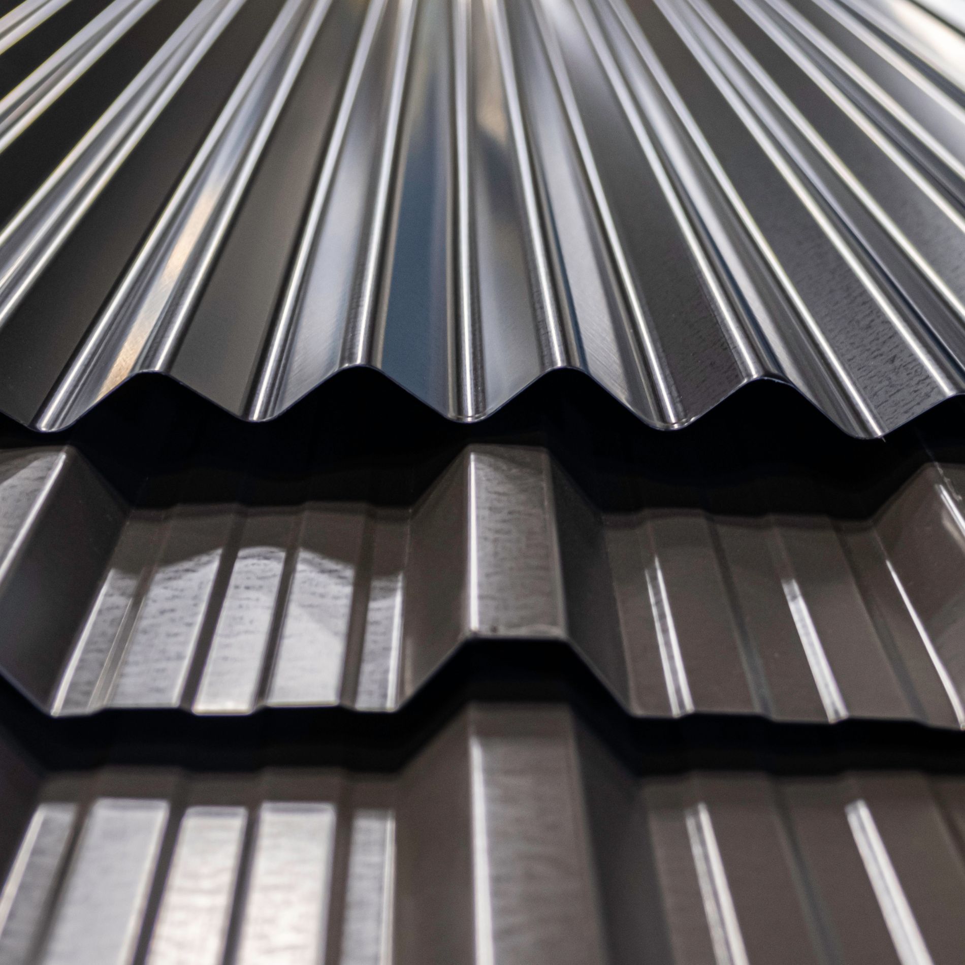 Close-up view of two sheets of corrugated metal roofing, one dark gray, the other dark brown.