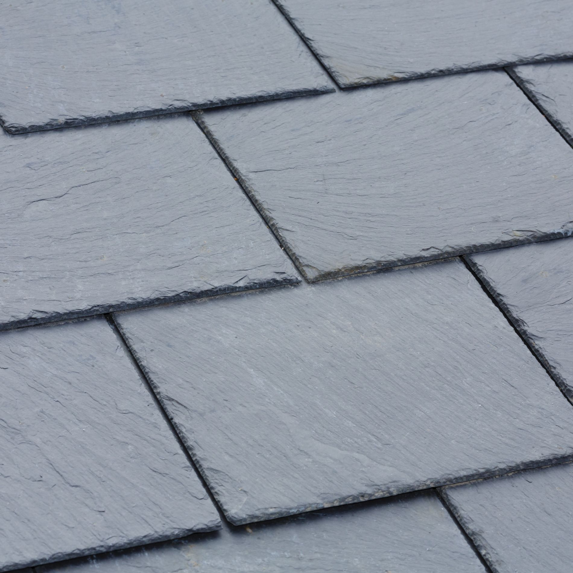 Close-up of gray slate roof tiles, overlapping and angled.
