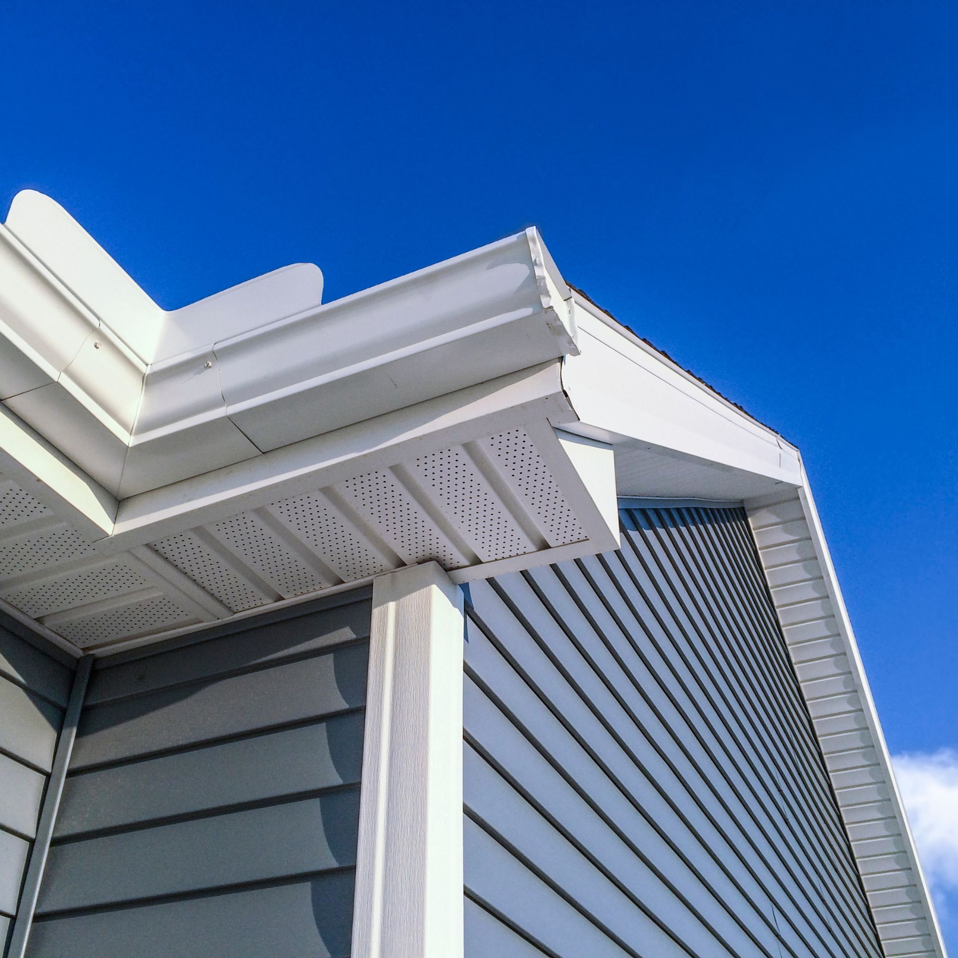 Corner of a house with blue siding, white trim, and a clear blue sky.