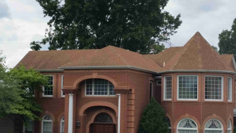 Brick house with arched windows and turret, red brick exterior and brown roof.