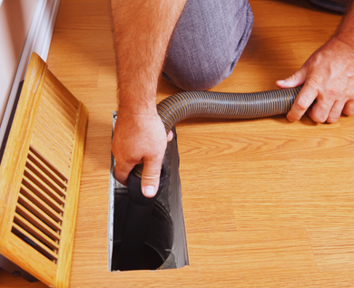 A man is using a vacuum cleaner to clean a vent on the floor