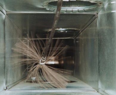 A brush is being used to clean an air duct