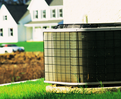 An air conditioner is sitting in the grass in front of a house