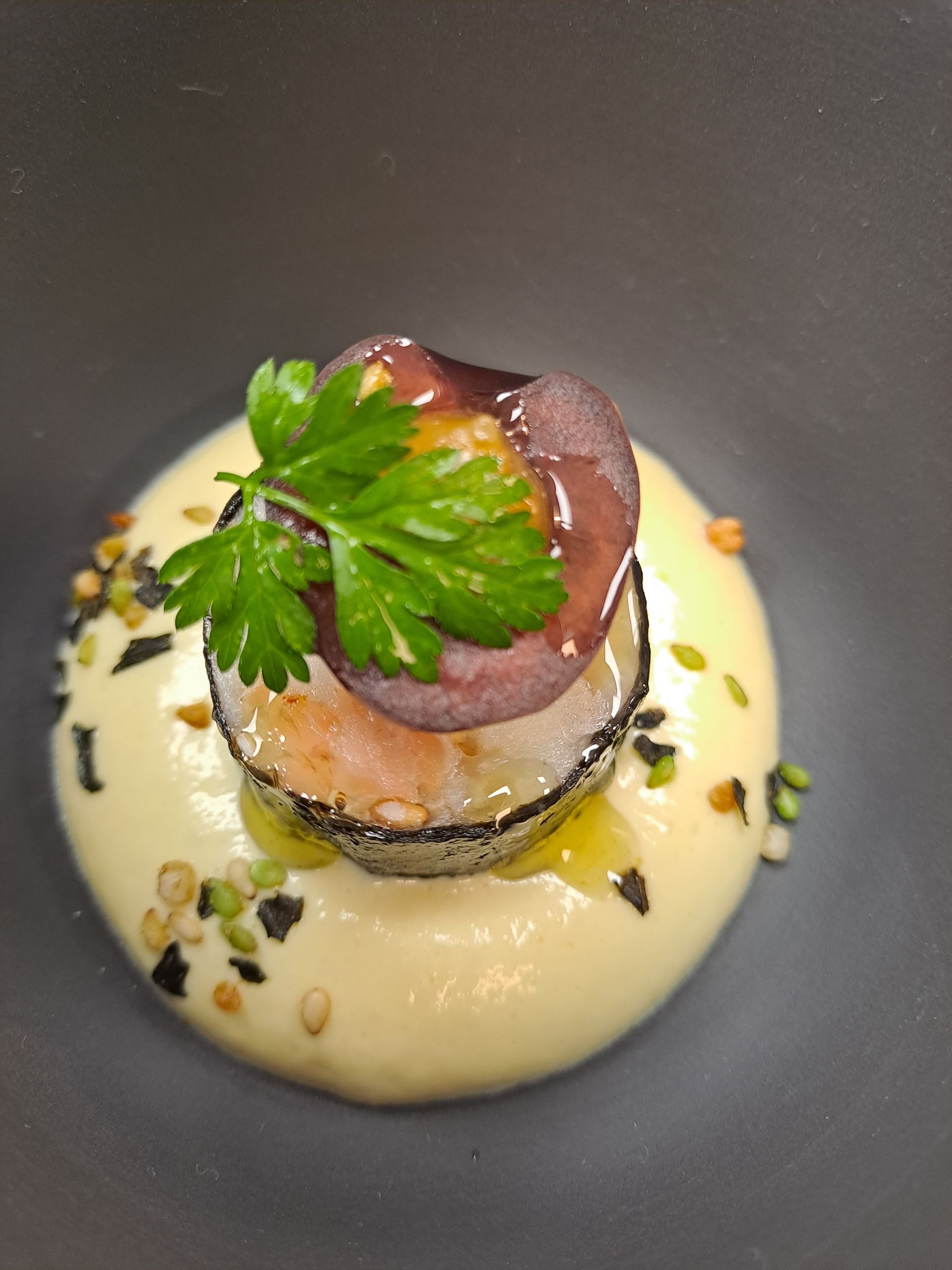 Creamy appetizer topped with fish, purple slice, parsley, and sprinkled seeds.