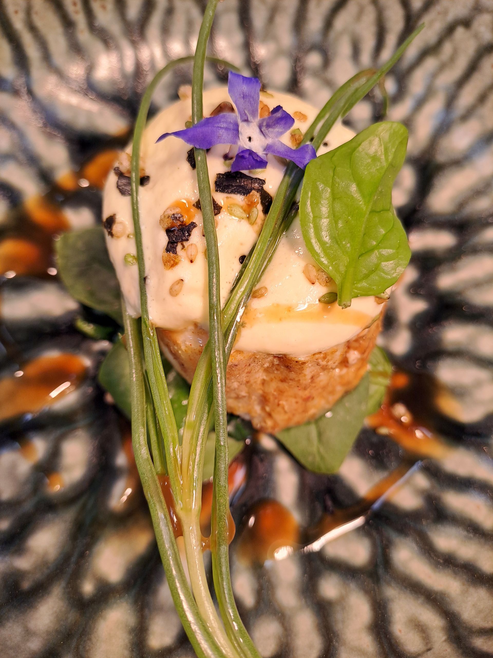 Elegant appetizer with cheese, herbs, and a purple flower, arranged on a decorative plate with sauce.