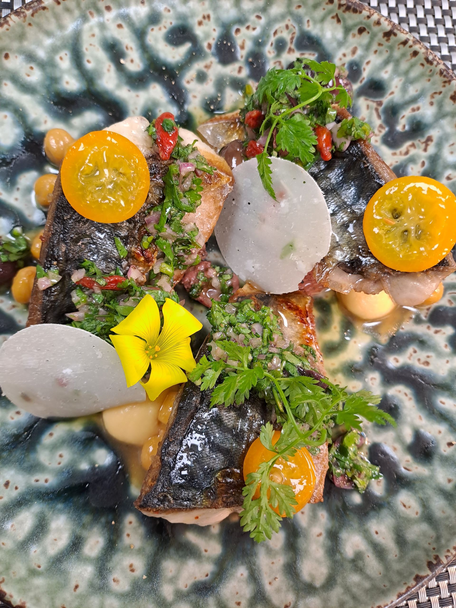 Pan-seared fish with yellow tomatoes, parsley, and radish on a decorative plate.