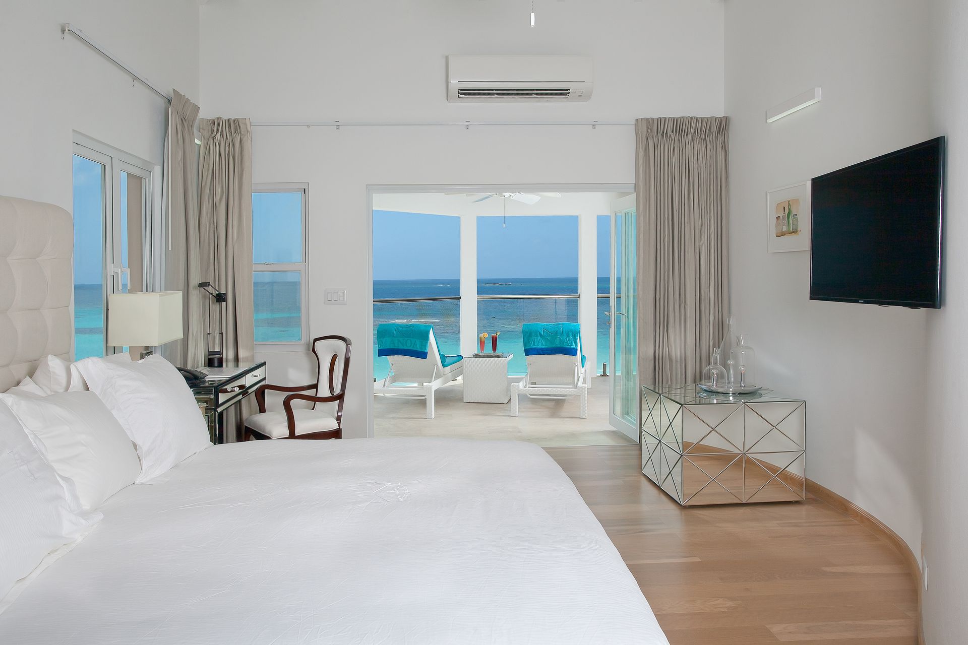 Bright bedroom with ocean view, king bed, balcony with lounge chairs.