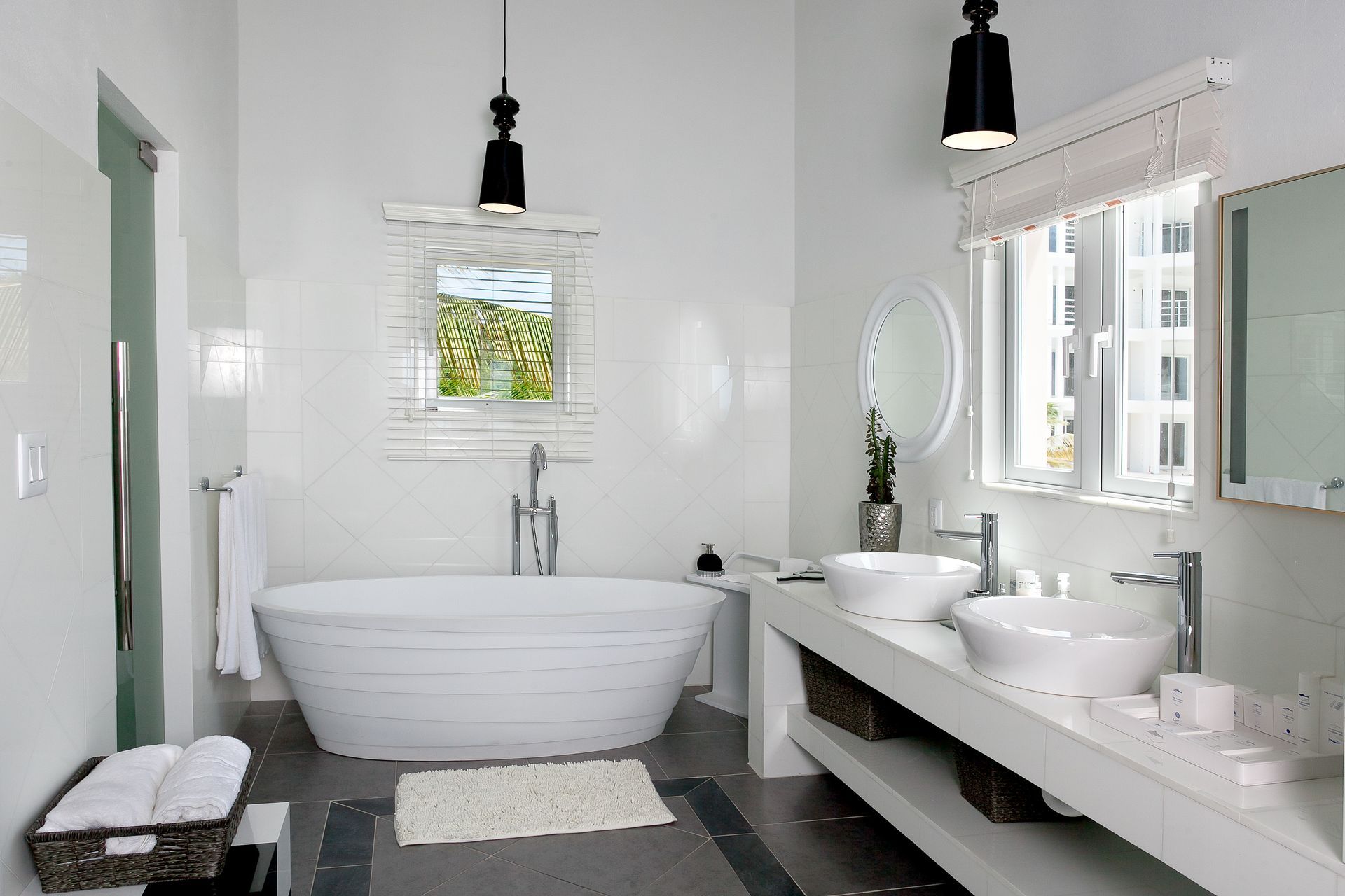White bathroom with a soaking tub, two sinks, and a small window.